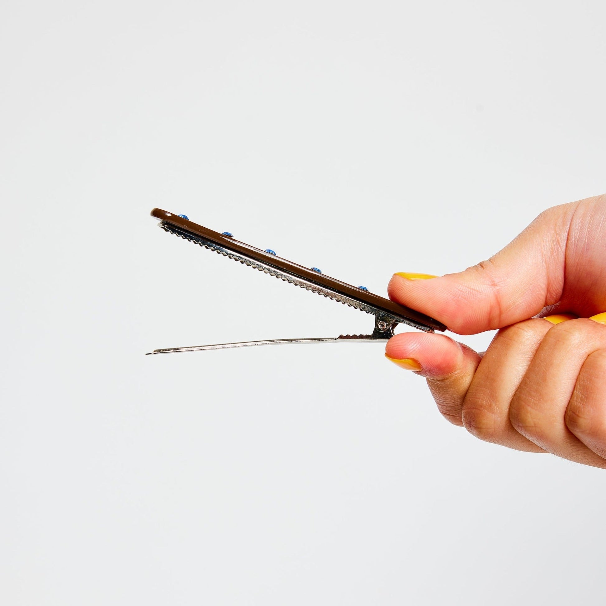 Hand opening a brown clip with blue rhinestones 