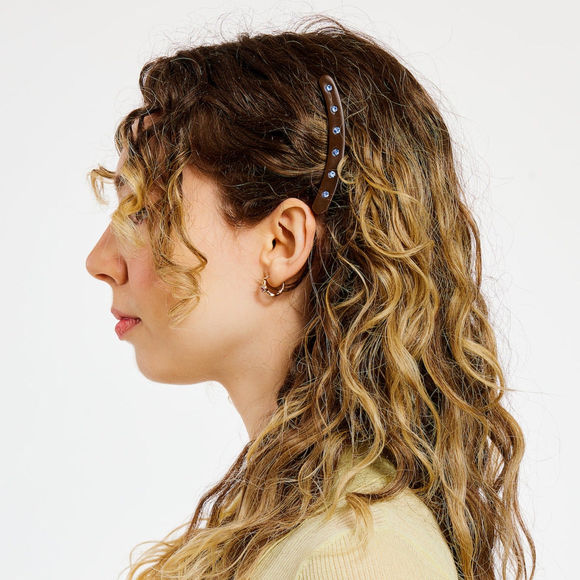 Woman with curly hair wearing a brown hair clip with blue rhinestones.