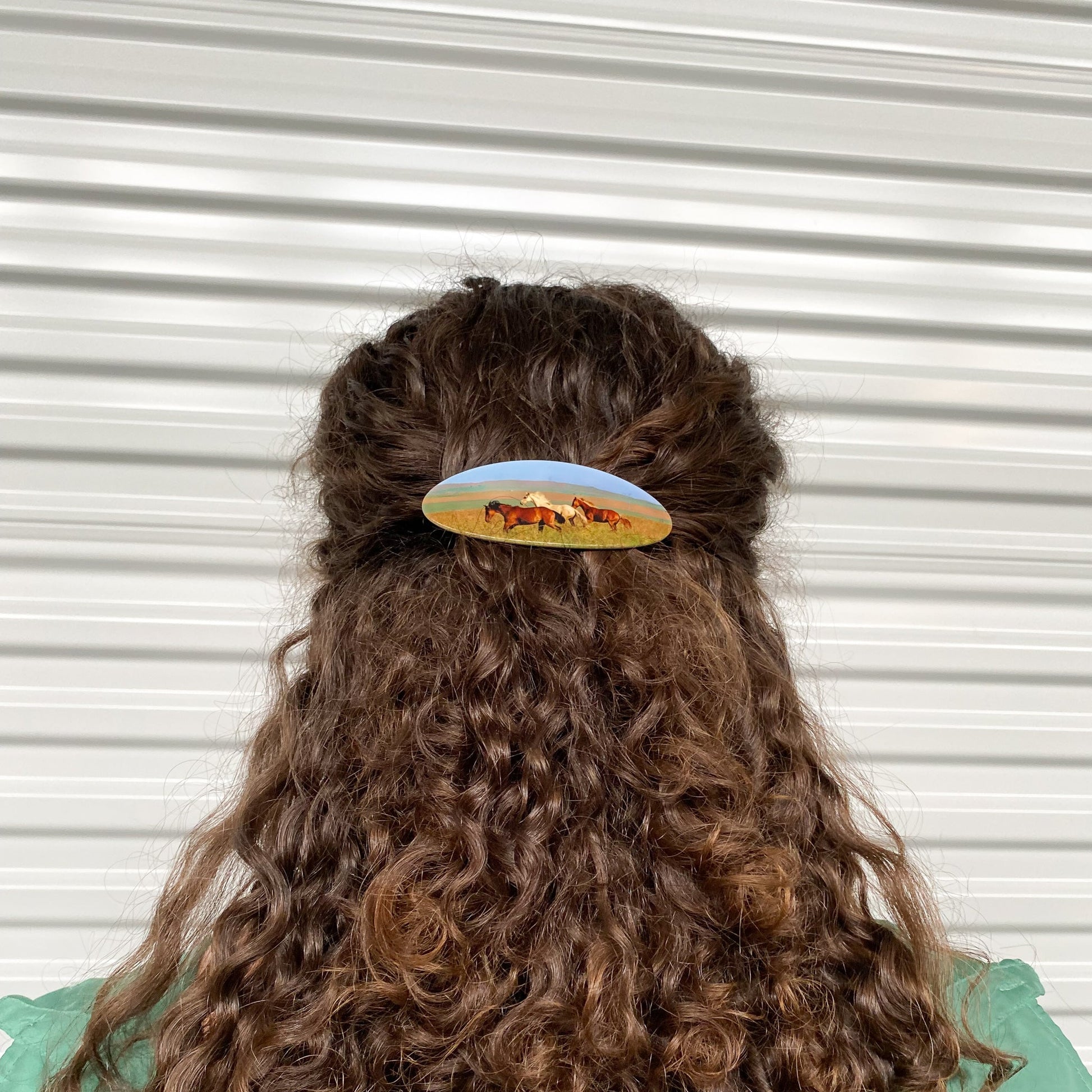 Hair barrette with printed horses worn on a brown curly hair.