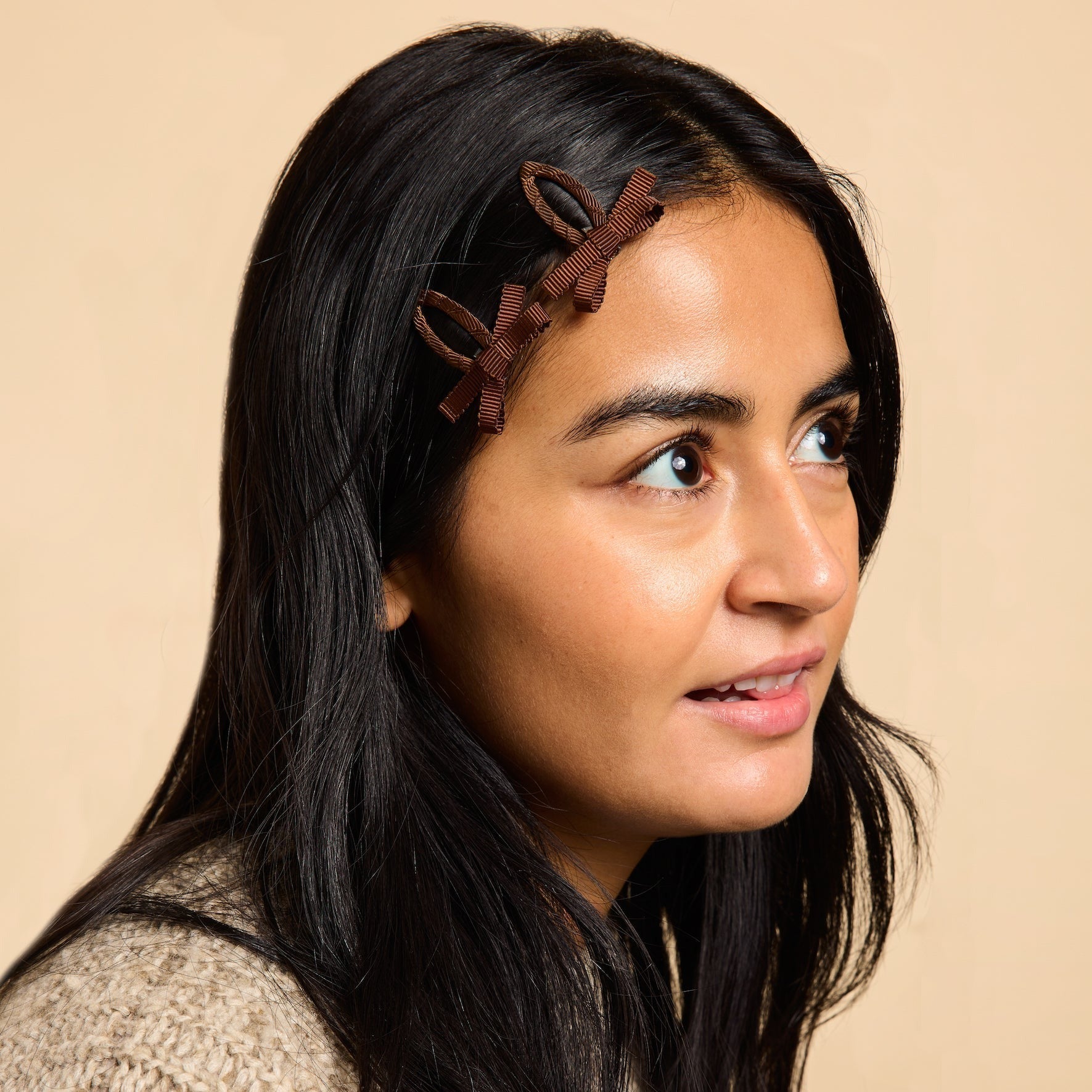 Woman with black hair wearing two brown bow snap hair clips.