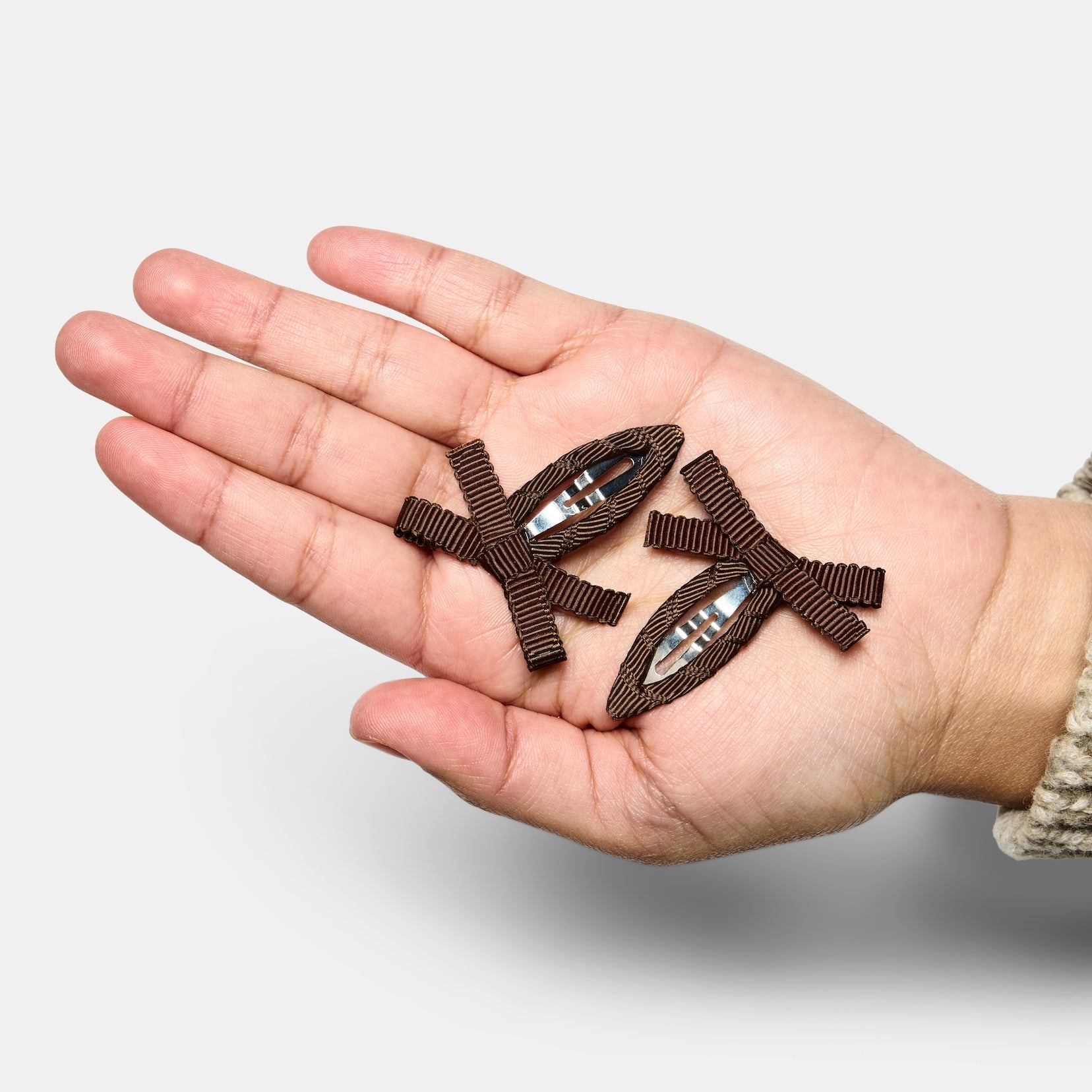 A hand holding two brown bow snap hair clips.