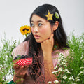 Woman wearing hair clips with fruits design,  posing with flowers and plants.