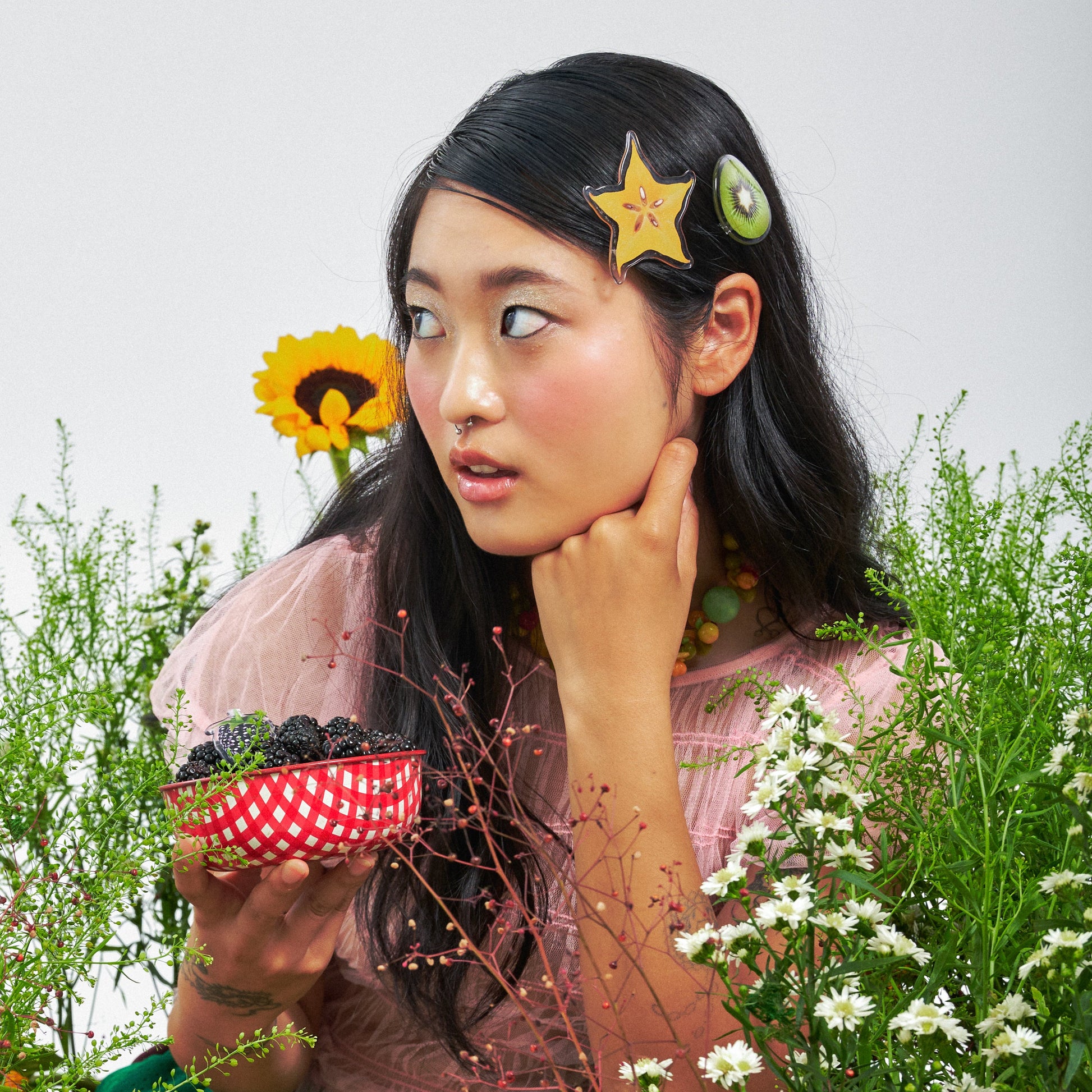 Woman wearing hair clips with fruits design,  posing with flowers and plants.
