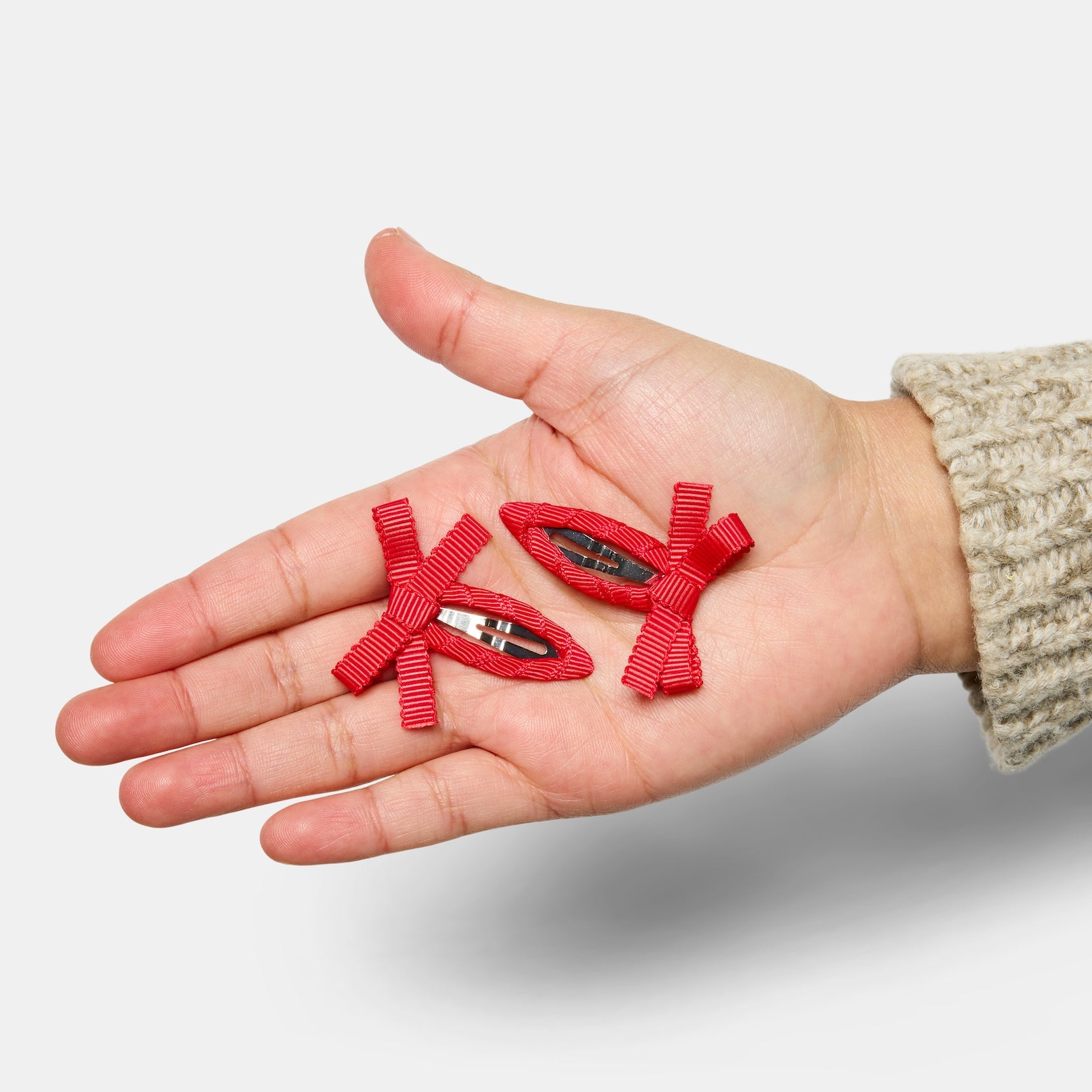A hand holding two red bow snap hair clips.