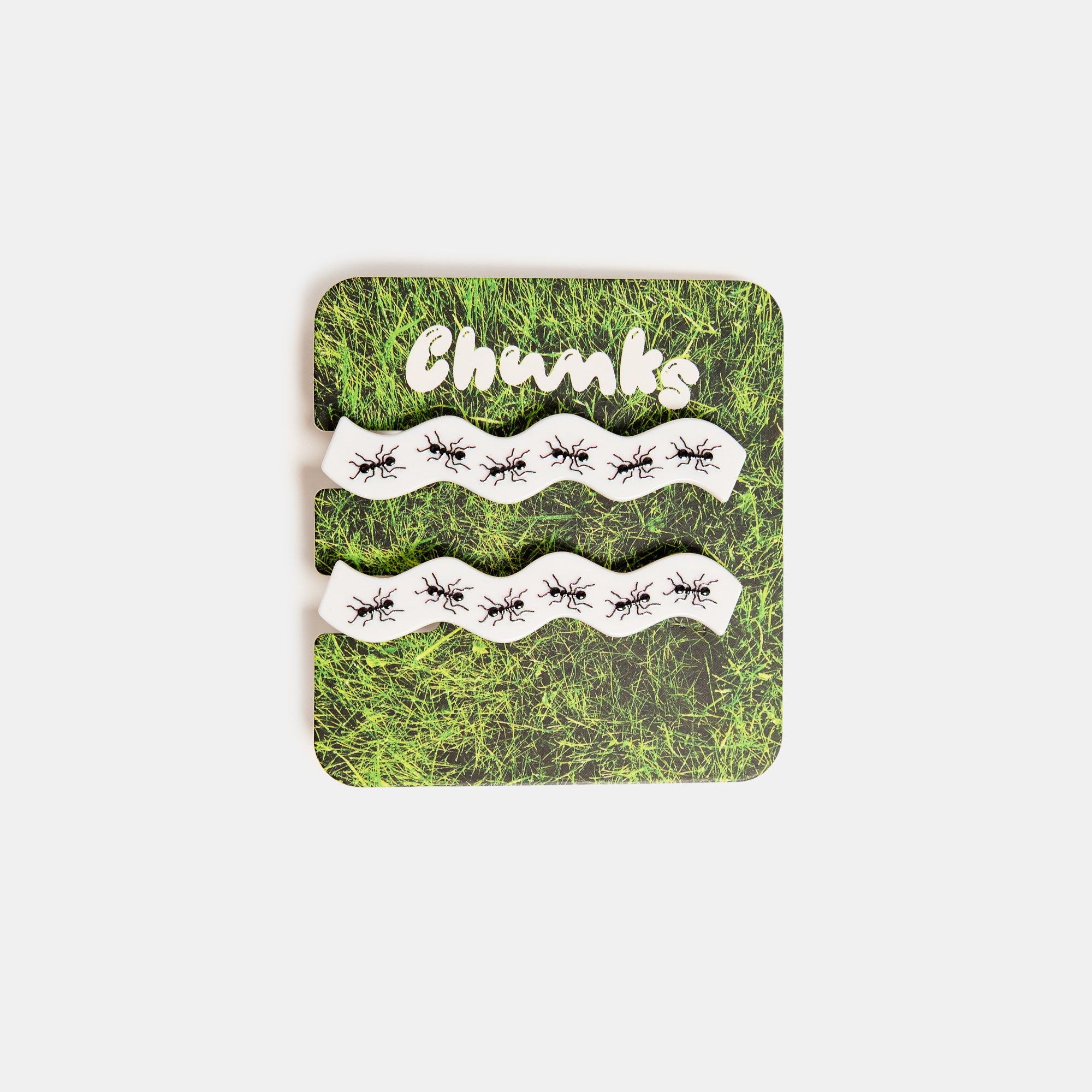 Two white hair clips with printed ants design clipped on a packaging card.