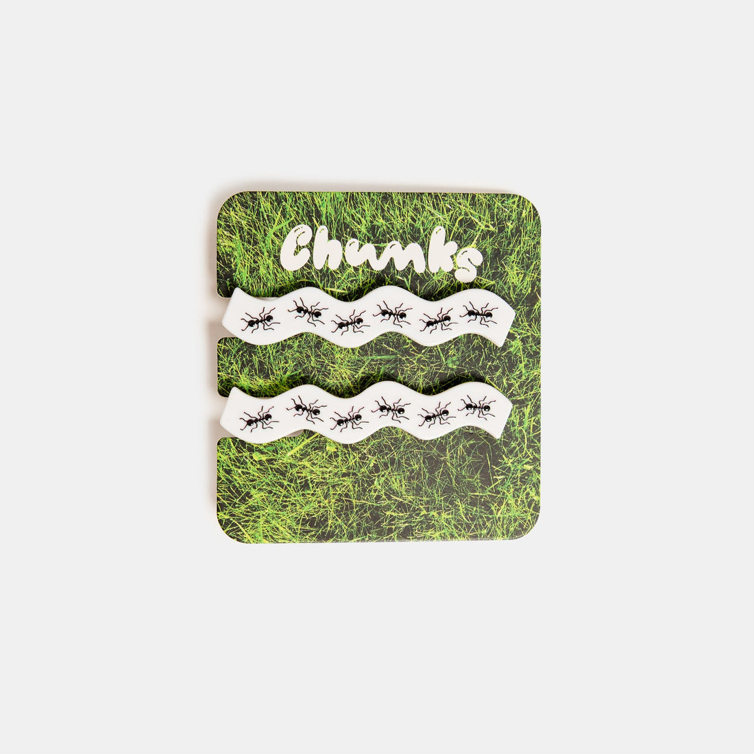 Two white hair clips with printed ants design clipped on a packaging card.