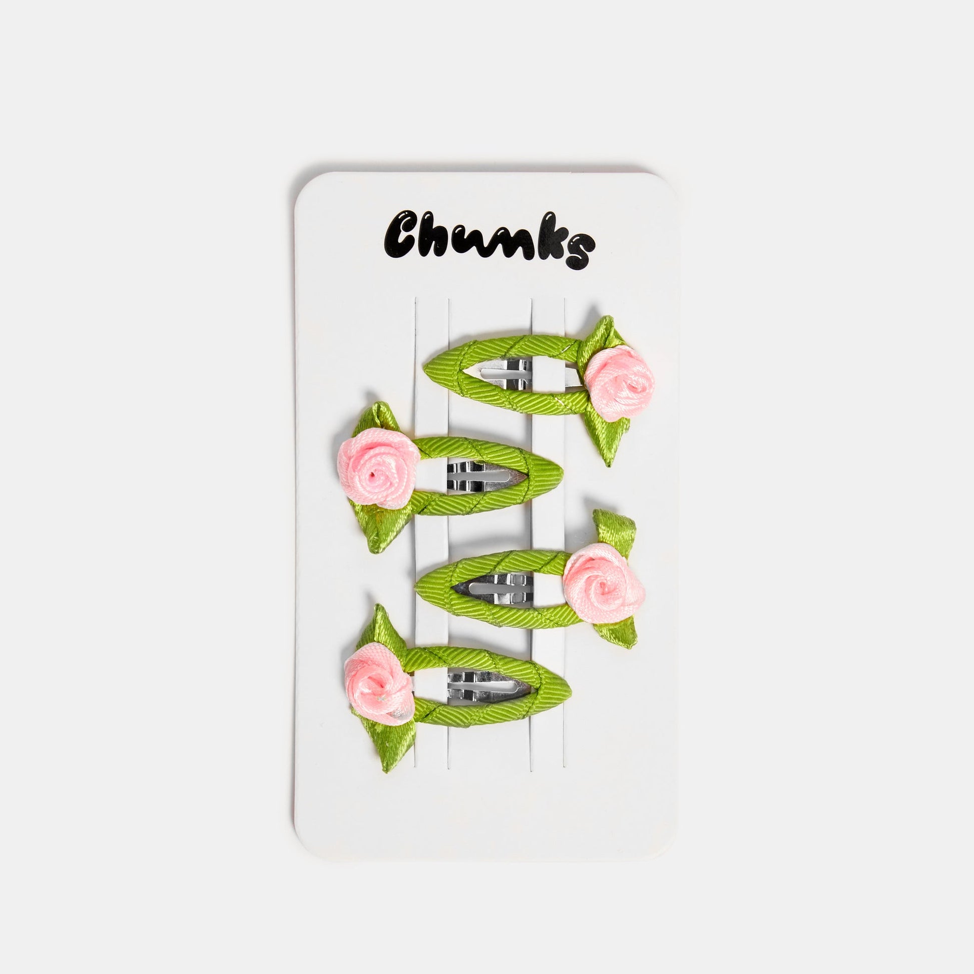 Four green and pink snap clips with rosette design on a white packaging card